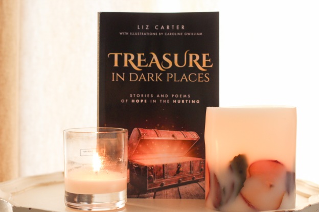 Two candles and a copy of Treasures in Dark Places by Liz Carter